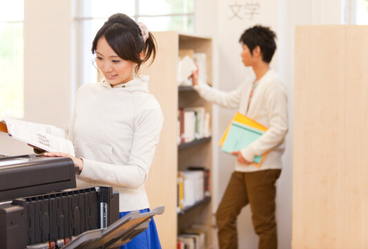 コピー機の前で本を開く女性