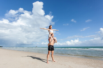 Happy young couple having fun at beach on sunny day, Happy man giving piggyback ride to his woman...