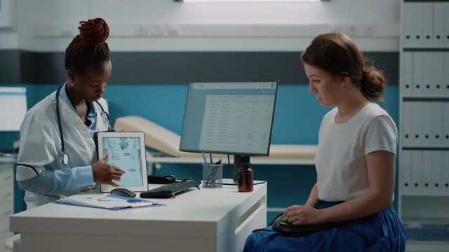 African american medic explaining bones fracture to patient at checkup visit. Black medic showing human skeleton image on tablet to young adult for osteopathy diagnosis and examination