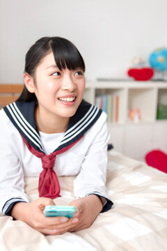 ベッドの上でスマートフォンを操作する女子校生