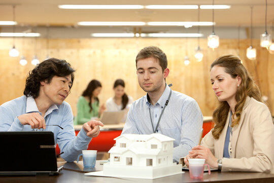住宅模型を見て話すビジネスマン3人