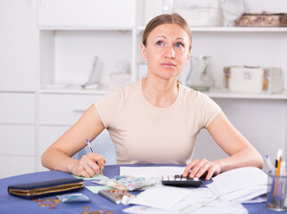 Upset woman calculating domestic finances with calculator and bills on table