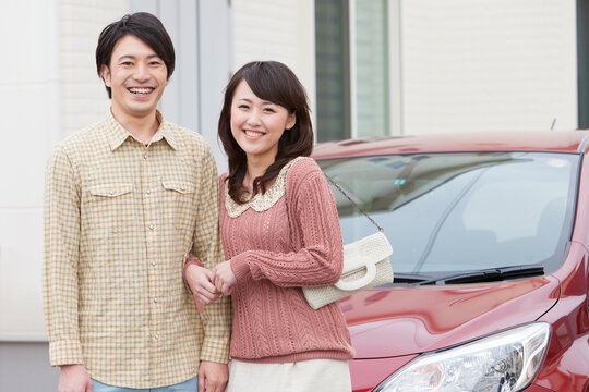 腕を組んでいる笑顔の夫婦と車