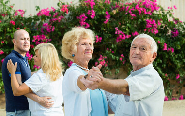 Glad cheerful positive adult friends dancing pair dance in garden