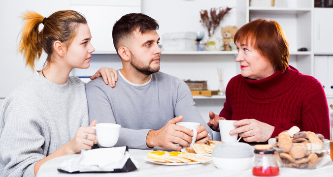 Senior Woman Having Serious Conversation With Young Couple Over Cup Of Tea At Home