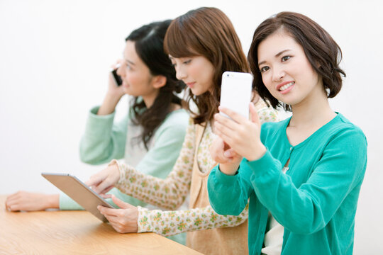 スマートフォン等を持つ女性3人
