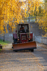 Fototapeta na wymiar Cleaning of leaves on the sidewalk with a tractor with a blade in autumn