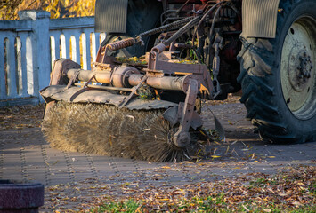 Cleaning dry wood in a city park with a tractor with a rotating broom