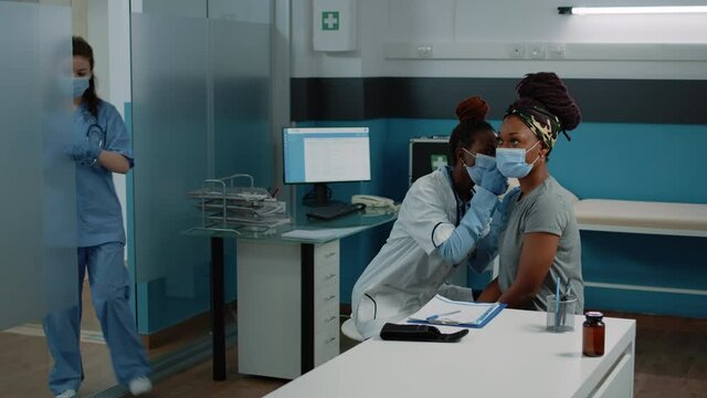 African american doctor using otoscope for ear examination of patient with face mask. Black medic and woman doing consultation for otology healthcare during coronavirus pandemic.