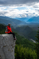 A female hiker on the rock overlocking the beautiful mountain valley, forest, clouds near Squamish BC, Canada. The light shines through the clouds