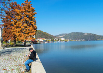 A man is looking closely at his smartphone. He was in the public park, on the shore of the lake, one autumn day. A beautiful landscape. Romania, Orsova. October, 20. 2021