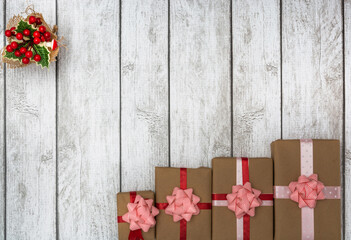 Holiday gifts wrapped in brown paper and holly on a white wooden background. New Year and Christmas concept. Flat lay
