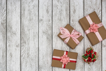 Holiday gifts wrapped in brown paper and holly on a white wooden background. New Year and Christmas concept. Flat lay