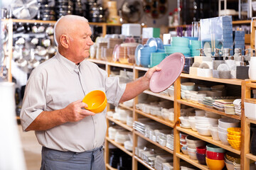 Attentive elderly man choosing new crockery in dinnerware store