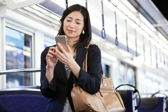 通勤電車でスマートフォンを操作するビジネスウーマン