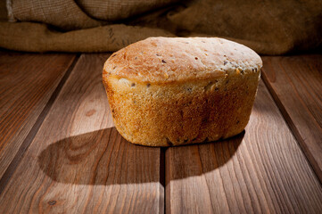 A loaf of delicious white bread made from natural products, on hops with flax saturation, without baker's yeast, on a wooden table surface.