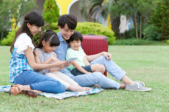 芝生でタブレットPCを見る4人家族