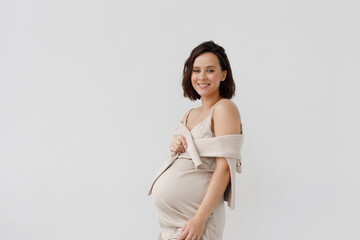 Fashionable portrait of a happy pregnant woman in an elegant dress. A young girl against a white...