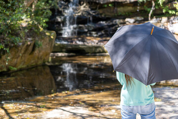 Lady from behind holding an umbrella to keep the sun off during a walk in the bush forest
