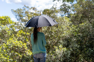 Lady from behind holding an umbrella to keep the sun off during a walk in the bush forest