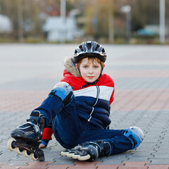 Little school kid boy skating with rollers in the city. child in protection safety clothes. Active...