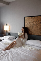 Beautiful morning of the bride in a light boudoir dress in a hotel on the bed. A young girl poses and smiles before the wedding.