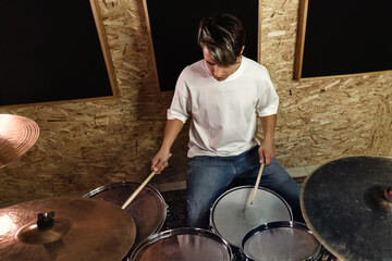 Active Rock musician artist beating rhythm is rehearsing behind a drum kit in studio. Authentic...