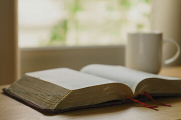 Close up of open bible with a cup of coffee for morning devotion on wooden table with window light. Christian background.