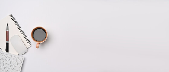 Above view minimal workspace with notebook, keyboard and coffee cup on white table.