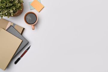 Coffee cup, potted plant and notebooks on white table. Copy space.