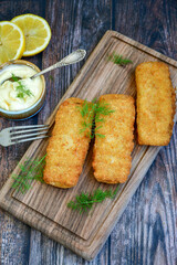 Close up of   Crispy breaded  deep fried fish fingers with breadcrumbs served  with remoulade sauce and  lemon Cod Fish Nuggets on rustic wood table background