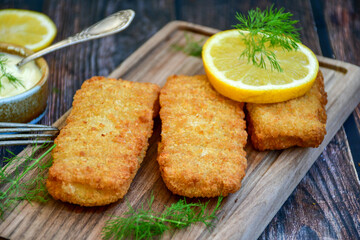 Close up of   Crispy breaded  deep fried fish fingers with breadcrumbs served  with remoulade sauce and  lemon Cod Fish Nuggets on rustic wood table background