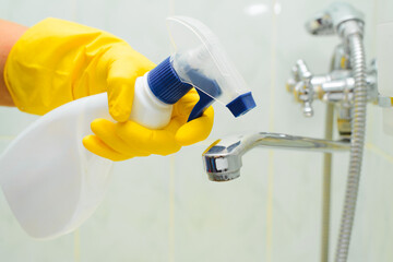Bath cleaning, disinfection and housework concept. Close-up of female hand in rubber glove holding antibacterial chemical spray, housewife cleaning faucet in bathroom