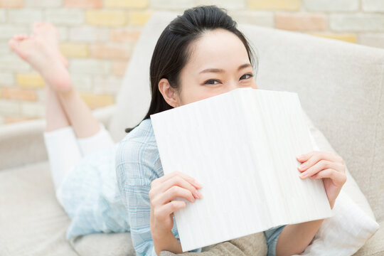 本で顔を隠す女性