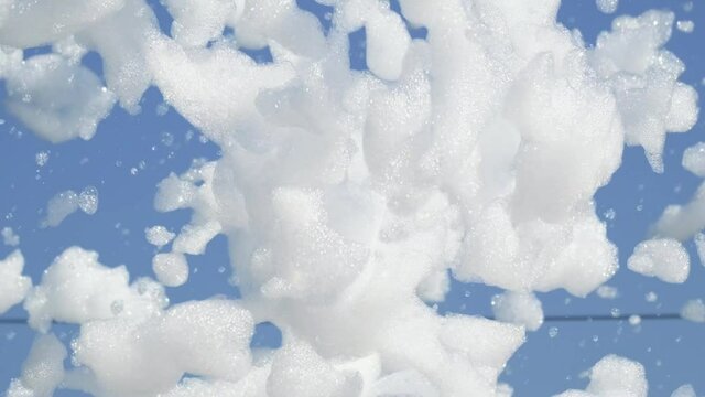 foam bubbles floating in the air in 4k slow motion.White soap foam on a blue sky background.