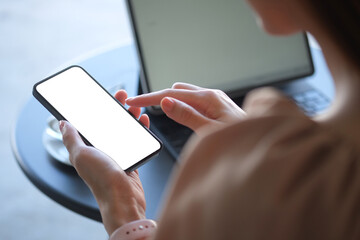 Young woman sitting in front of computer laptop and using smart phone.