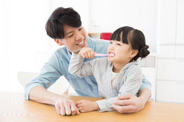 父親の膝の上で歯磨きする女の子