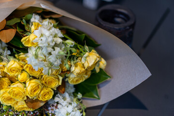 Bouquet of soft yellow roses and white flowers, wrapped in brown kraft paper
