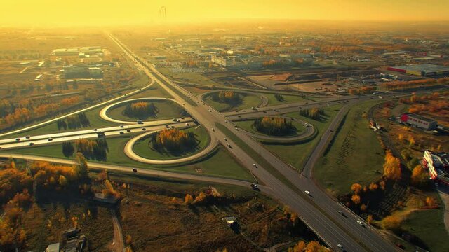 Beautiful symmetrical road junction, cloverleaf interchange, surreal aerial flight in the early morning light of the rising sun, mesmerizing movement of cars along the road.