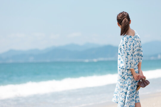 サンダルを持って海を眺めている女性