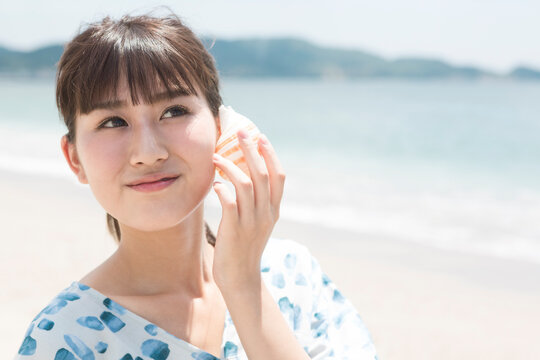 貝を耳に当てている女性