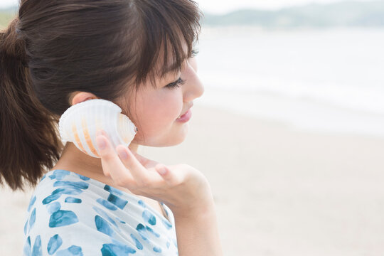 貝を耳に当てている女性