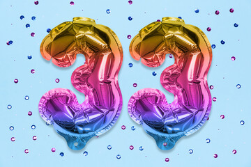 Rainbow foil balloon number, digit thirty three on a blue background with sequins. Birthday greeting card with inscription 33. Top view. Numerical digit. Celebration event, template.