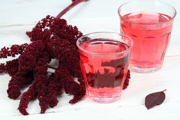 Herbal tea from blood amaranth. Amaranthus cruentus tea used  for unique taste. Glass and flower on white wooden table. Grown for nutrient seeds in Central America.