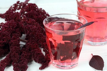 Herbal tea from blood amaranth. Amaranthus cruentus tea used  for unique taste. Glass and flower on white wooden table. Grown for nutrient seeds in Central America.