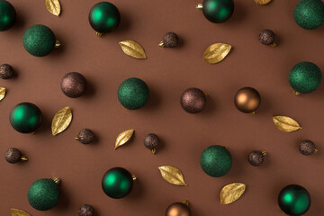 Top view photo of green brown golden christmas tree balls and golden leaves on isolated brown background