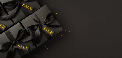 Top view photo of black gift boxes with black satin ribbon bow and golden confetti on isolated black background with copyspace
