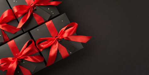Top view photo of black gift boxes with red satin ribbon bow on isolated black background with copyspace