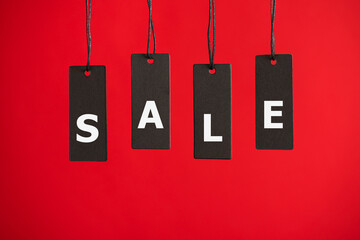 Photo of hanging black price tags on isolated red background with text letters sale