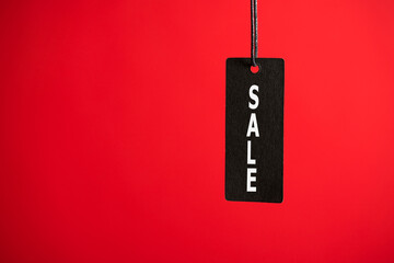 Photo of hanging black price tag on isolated red background with text sale